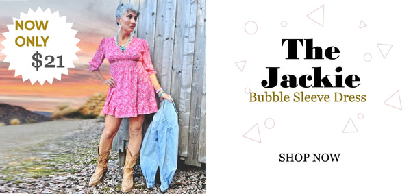 A woman standing in front of a wooden barn in a pink floral minidress and tan cowboy boots