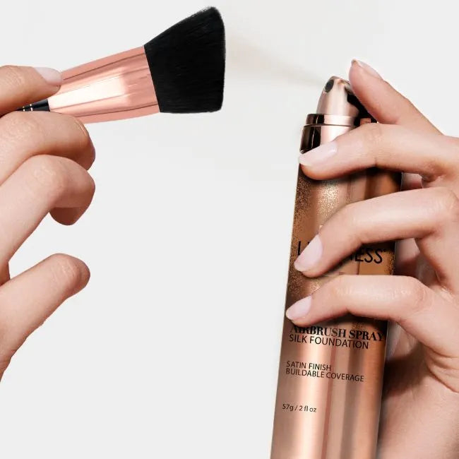 Hands holding a makeup brush and an airbrush spray foundation.