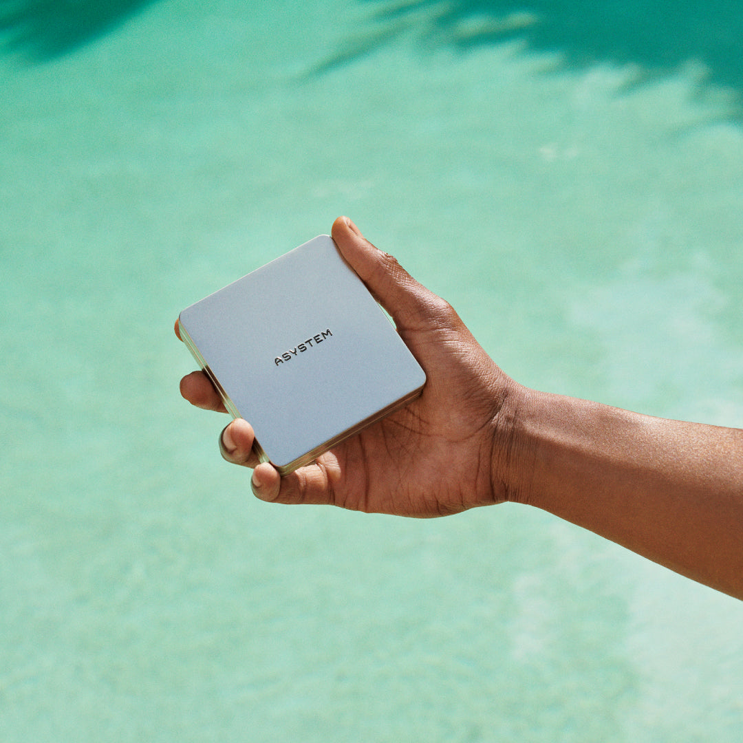 A hand holding a square ASYSTEM product case in front of a pool.