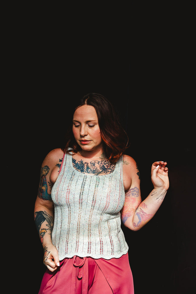 Elizabeth stands against a black background in coral tie front pants and a light gray lace hand knit tank top