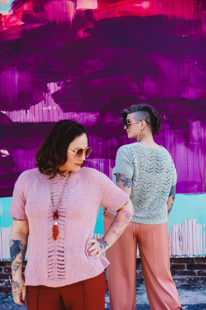 In the foreground, Bess is blurry wearing a longer pink silk knit tee with lace panels, Jen displays the back of her mint green Silk tee with a lace back which she has knit shorter.