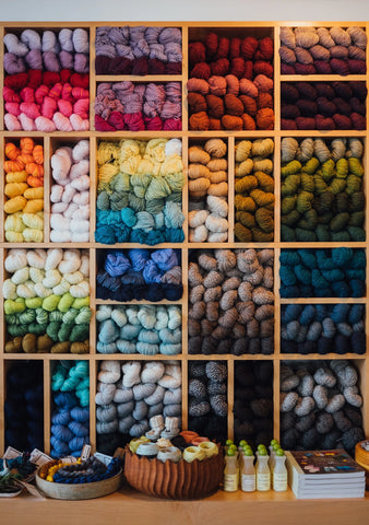 A wall of yarn, organized by colour in cube shelves.