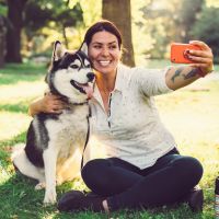 Photo of a woman sitting in a park and taking a selfie of her and her husky.