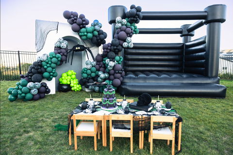 Kid's Halloween Party Setup with Black Bounce Castle, Black, Green, and Purple Balloons, and Picnic Table