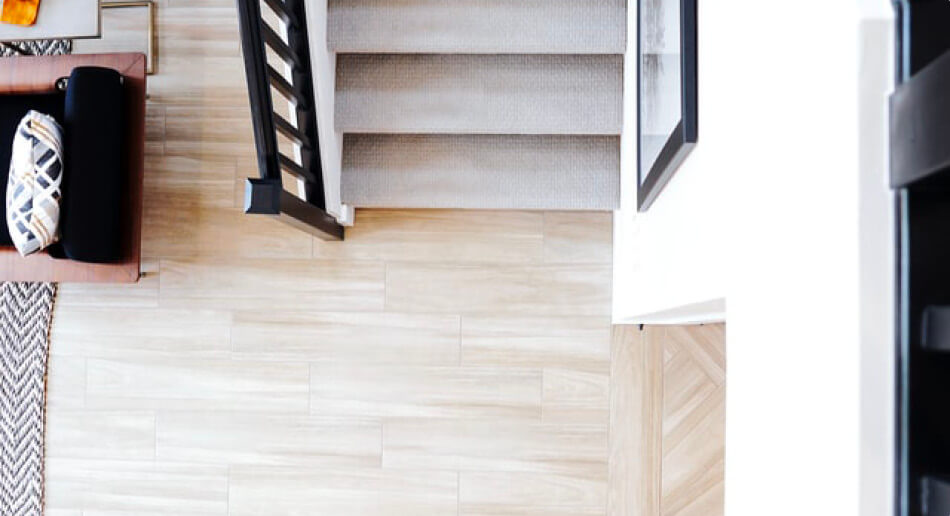 top down image of a light real wood floor and a carpeted stairs