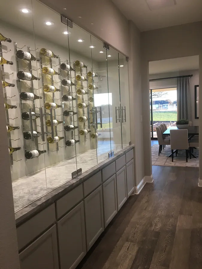 Glass enclosure of metal wine racks above built-in cabinets in a hallway with dining table visible through a doorway