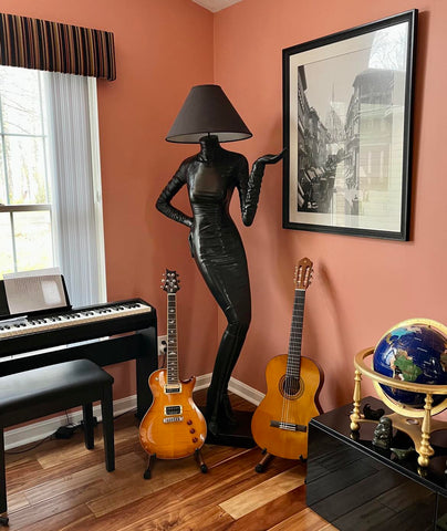 Two guitars on stands next to lamp and piano. 