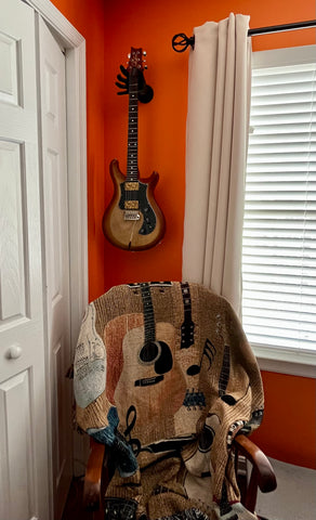 PRS guitar with hand guitar hanger on orange wall.