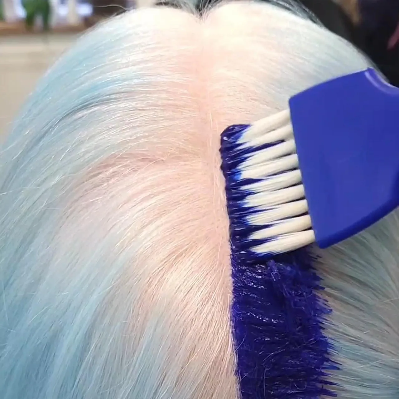 A hairstylist is applying blue hair dye to his client