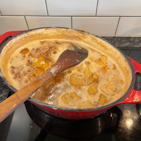 Red cast iron pot full of feijoa fruit, simmering away with a wooden spoon resting on top