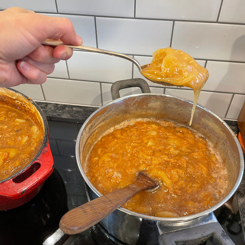 Hand holding a spoon heaped with golden honey, ready to go into a big pot of cooked feijoas