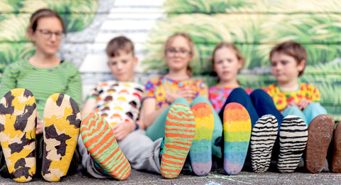 Hoopla Kids sitting against a wall in the late afternoon, wearing Paper Krane shoes showing the range of coloured soles