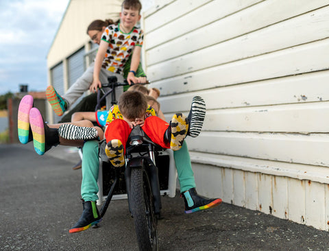 Lots of kids piled into a cargo bike, wearing Paper Krane footwear and bright clothes from Hoopla Kids