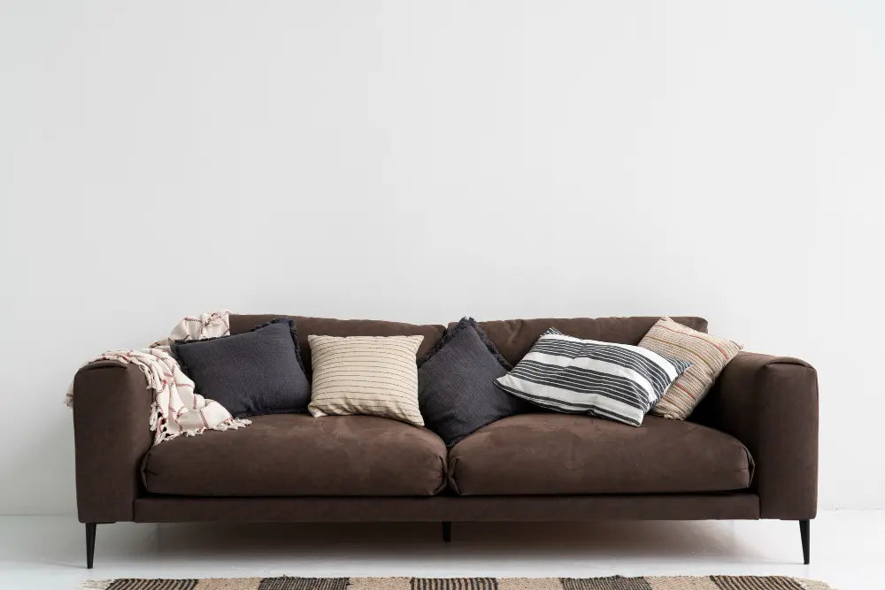 photo d'un canapé marron deux places, avec des coussins gris et beige