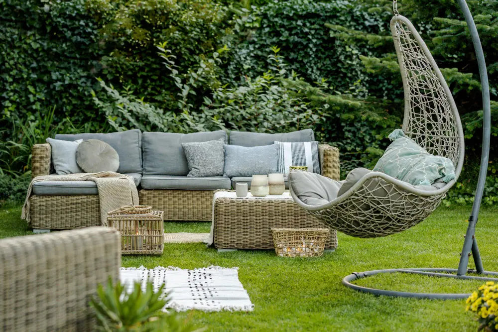 Photo d'une terrasse en osier avec un canapé gris, une table en osier, un siège suspendu, une pelouse, un tapis blanc 