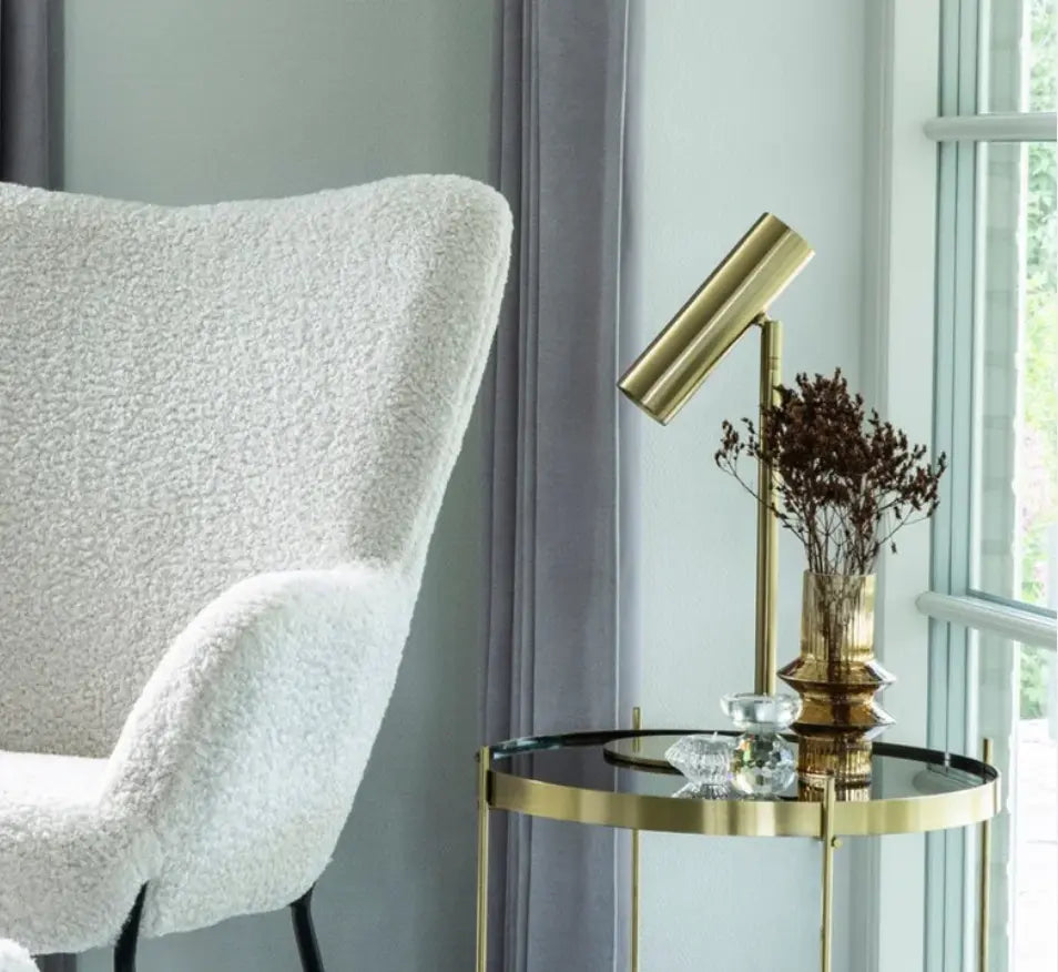 luminaire or pour salon sur une table basse en verre à coté d'un fauteuil de salon blanc