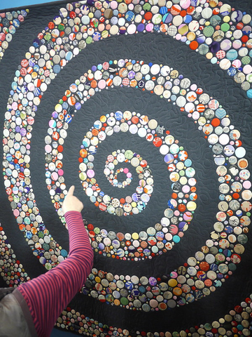 Image shows a modern quilt made of small circles placed on a gray background to form a spiral.