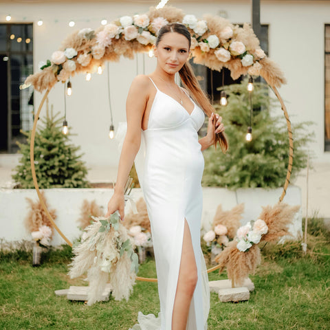 A bride standing in front of a large circular alter feature that has been dressed in pampas grass and flowers.