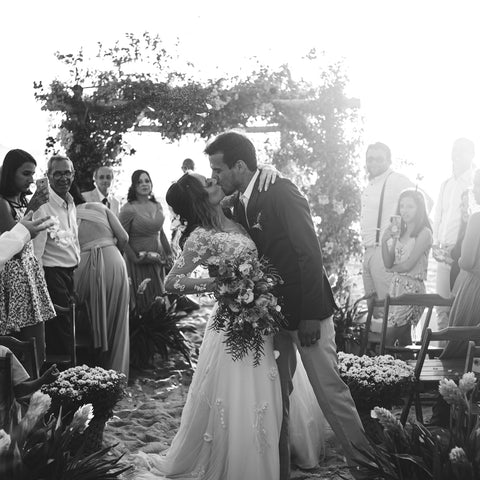 A wedding couple and their party outside, surrounded by flowers.