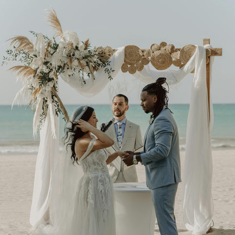 A beach wedding scene with an alter decorated with pampas grass and green foliage.