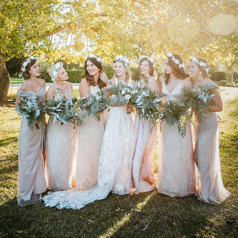 A bride with her bride's maids standing with their bouquets and flower crowns in the sunshine.