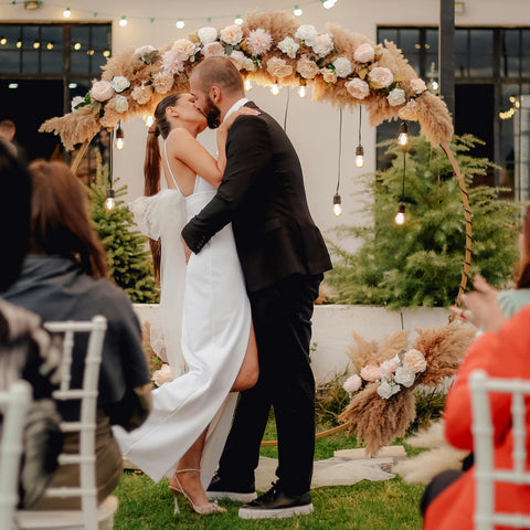 A newly married couple kissing in front of a circular floral alter piece.