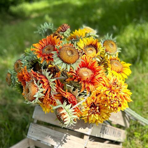 A group of different coloured, sized, and shaped faux sunflowers, displayed in a meadow against a bright, sunny sky