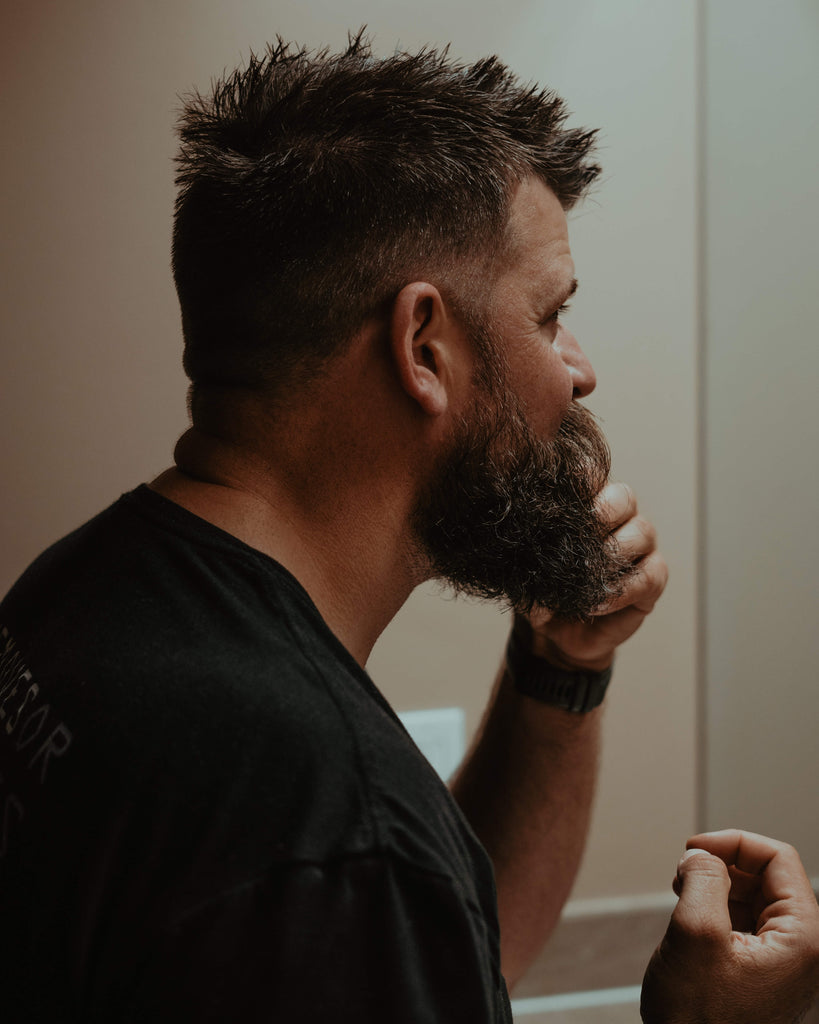 man looking in mirror and styling with beer products for beard growth