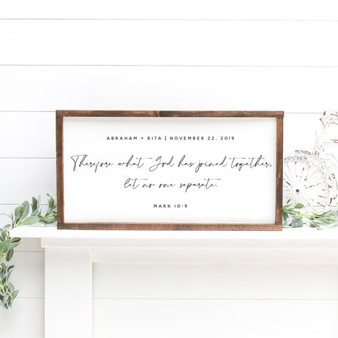 Custom Wedding Scripture Canvas framed with dark wood, displaying names 'Joshua & Stella', date 'December 2, 2018', and a verse from I John 4:12. Positioned atop a white mantel, with decorative elements and greenery on the side.