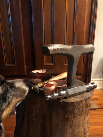 Interior shot shows a tree stump with metal forming tools and copper bowls on it