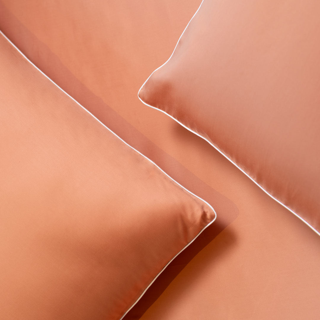 Two blush-colored pillows with white piping on a matching sheet.