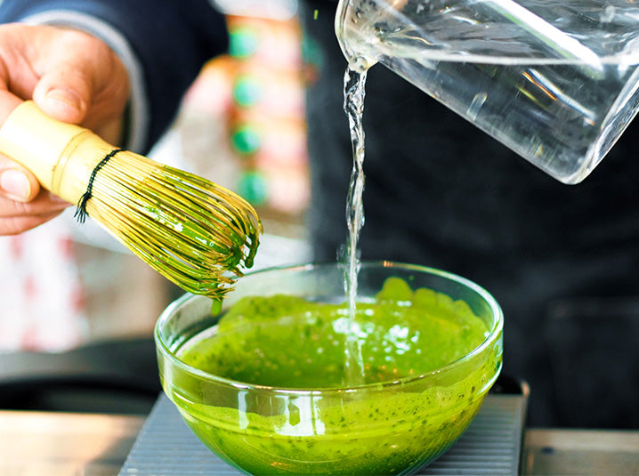 preparing traditional koicha technique matcha green tea in a glass bowl whisking with a bamboo whisk while pouring water