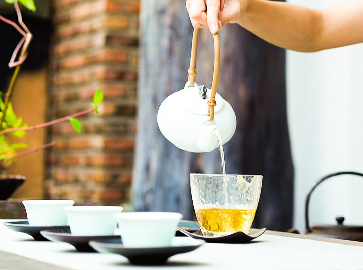 pouring yuzu japanese fruit tea from a white kyusu to a glass yuzamashi with white tea cups lined up