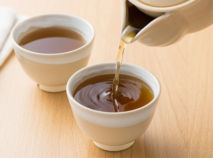 hand pouring senbird organic hojicha roasted green tea into tea cups