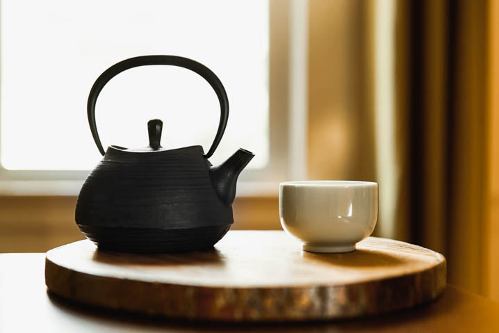 a glass cup of tea next to a teapot on wooden tray