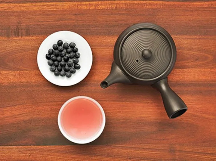 caffeine-free japanese kuromame black bean herbal tea on a white plate with a brewed cup and kyusu teapot on a brown wooden table