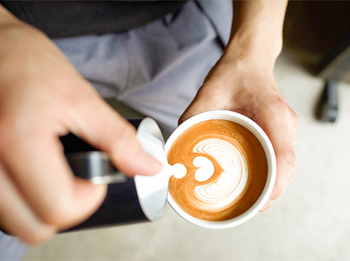 Barista pouring steamed milk into white cup of coffee with caffeine to make coffee latte art