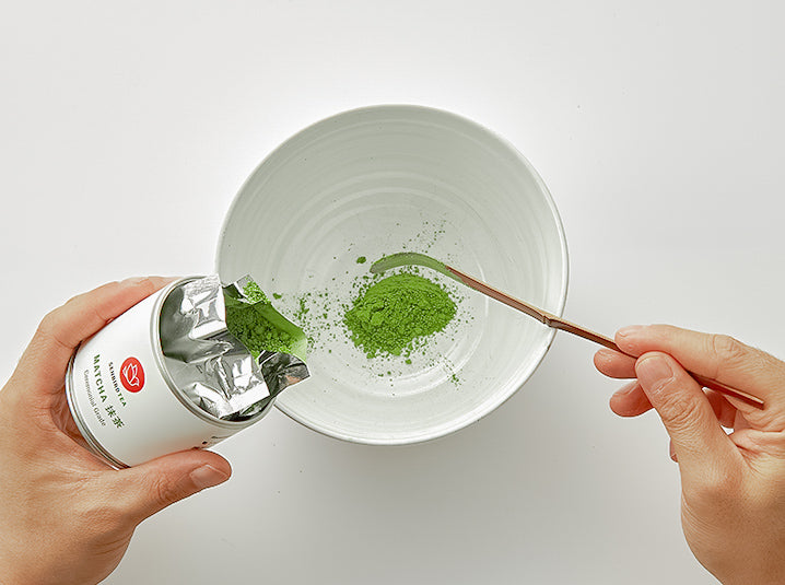 scooping senbird ceremonial matcha otome from the tin using bamboo scoop pouring it into the white matcha bowl