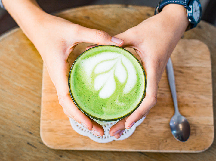 two hands holding matcha latte with caffeine content creating a beautiful leaf latte art