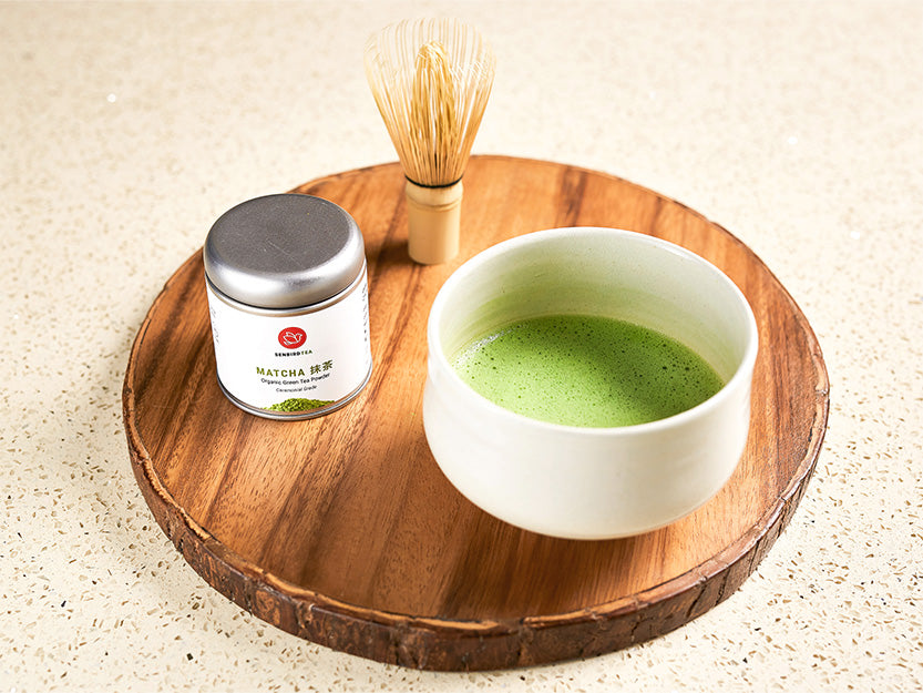 brewed Matcha in cup with matcha tea tin and bamboo whisk