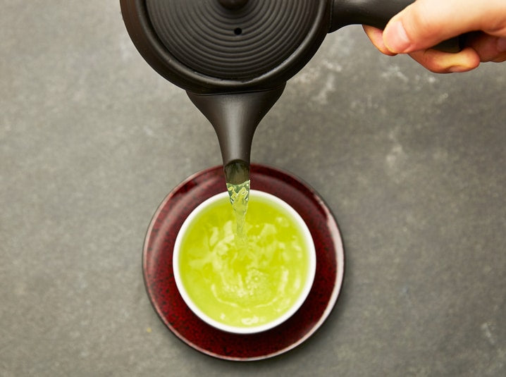 hand pouring senbird organic Japanese sencha green tea into tea cup