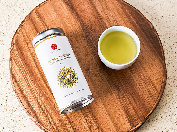 senbird's genmaicha japanese brown rice tea mixed with sencha and matcha tin with a brewed genmaicha in a teacup beside on top of a wooden board