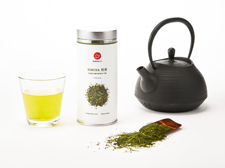 Brewed sencha in a glass with sencha tea tin and teapot