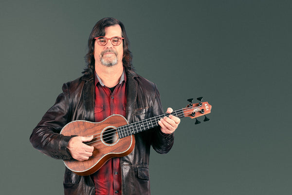 A man (Mike Upton) holds a Koa U•BASS® with Abalone rosette in front of a greyish green background