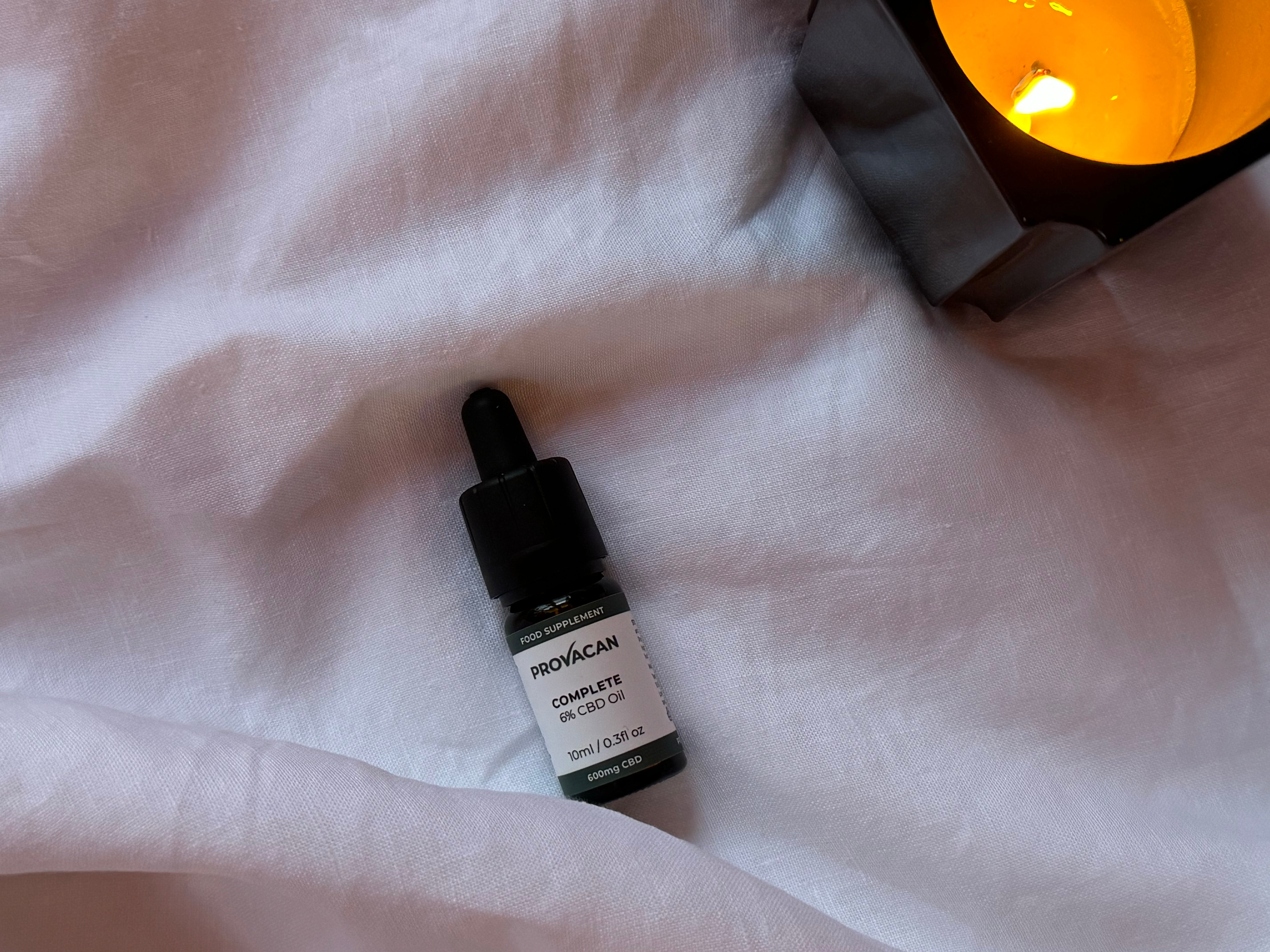 A bottle of Provacan CBD oil beside a glowing candle on white fabric.