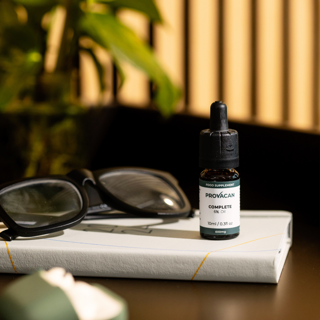 A bottle of Provacan CBD oil on a book beside eyeglasses.