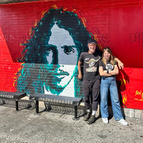 Anita Stelmasiuk with Matt Vaughan from Easy Street Records standing next to a vibrant mural of Chris Cornell on a red brick wall in Seattle, painted by local artist Son Duong.