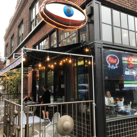 The front view of Cyclops Cafe in Belltown, Seattle, with its unique eye-shaped sign and neon lights, a popular spot for local musicians.