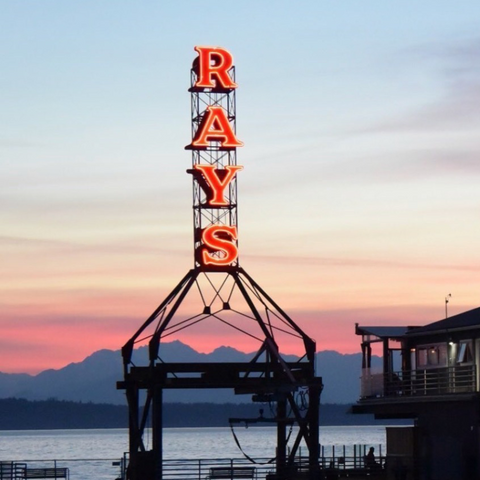 Ray's Boathouse sign illuminated at dusk with a stunning backdrop of the Puget Sound and distant mountains in Seattle.