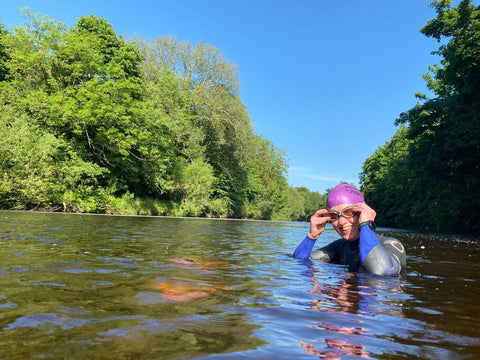 swimmer adjusting goggles in river with trees and blue sky beyond
